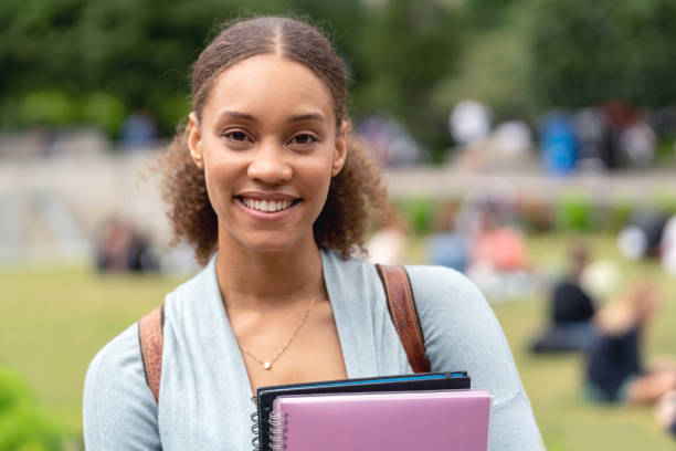 Portrait of an African American female student holding notebooks outdoors and looking at the camera smiling - education concepts