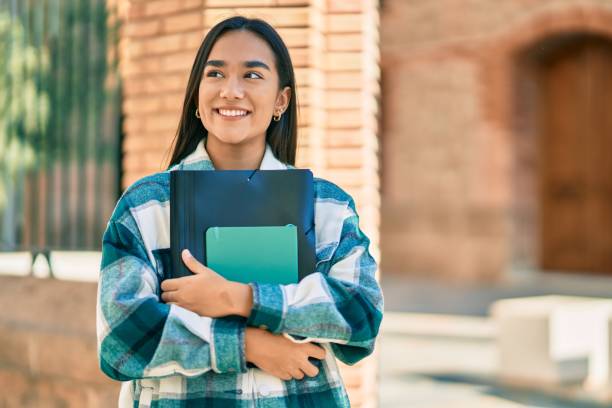 Young latin student girl smiling happy holding folder at the city.